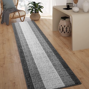 May include: A gray and white striped runner rug with a geometric pattern. The rug is laid out on a hardwood floor in a home.