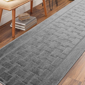 May include: A gray runner rug with a brick pattern. The rug is laid out on a hardwood floor.