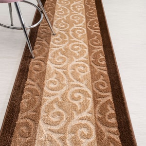 May include: A brown and beige patterned runner rug with a brown border. The rug has a floral design.