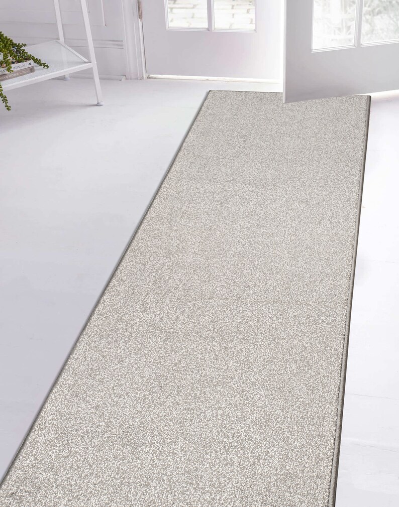 May include: A light gray runner rug with a subtle textured pattern. The rug is placed in front of a white door.