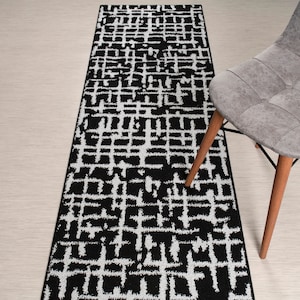 May include: Black and white geometric patterned runner rug. The rug has a modern abstract design with a black background and white lines.