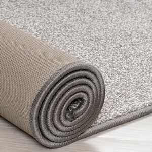 May include: A close-up of a rolled-up gray and beige rug with a gray border. The rug is made of a soft, plush material.
