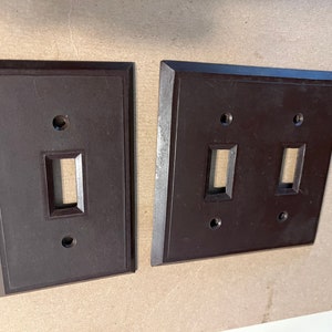 May include: Two vintage brown plastic light switch plates. One plate has a single switch and the other has two switches.