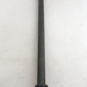 May include: A long, slender, dark metallic rod with a smooth cylindrical shaft. The top features an ornate, scroll-like decorative handle, while the base terminates in a flared, rounded pedestal foot with a small circular opening at the center.