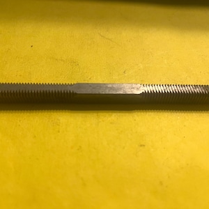 May include: A metal file with a ridged, cylindrical design. The tool is silver in color and lies horizontally against a yellow background. The file is used for shaping and smoothing materials.