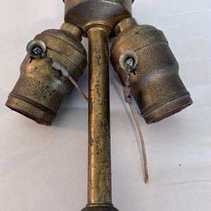 May include: Vintage brass ceiling light fixture with three bulb sockets. The fixture has a central stem with a decorative base and a circular top. Each socket has a pull chain.