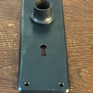 May include: Black metal door plate with a keyhole and a round hole for a door knob.