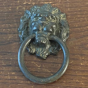 May include: A vintage lion head drawer pull with a ring handle. The pull is made of metal and has a dark brown finish.