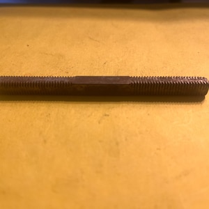 May include: A brown metal tap and die tool with a ridged surface. The tool is cylindrical with a flat, unridged section in the middle. The tool is used for cutting threads.