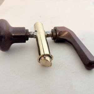 May include: A door hardware assembly featuring a dark brown, rounded knob on one side and a matching dark brown lever handle on the other. These components are connected by a central, polished brass-colored cylindrical mechanism.