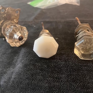 May include: Three vintage cabinet knobs. One knob is clear glass with a metal backplate. Another is a white, faceted knob. The third is a clear, faceted glass knob with a metal base. All knobs have metal stems.