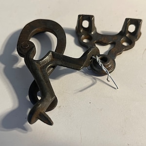 May include: A rusty metal latch with a hook and a bracket. The latch is designed to secure a door or gate.