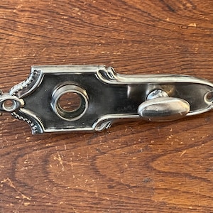 May include: A silver door knob with a decorative design and a round keyhole. The knob is attached to a rectangular plate with a decorative edge.