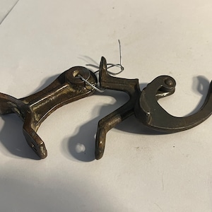 May include: A vintage metal window latch with a hook and a lever. The latch is made of dark metal and has a worn, rustic look.