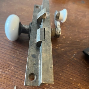 May include: A vintage metal door latch with a white porcelain knob and a lever handle. The latch has a silver finish and is designed for a sliding door.