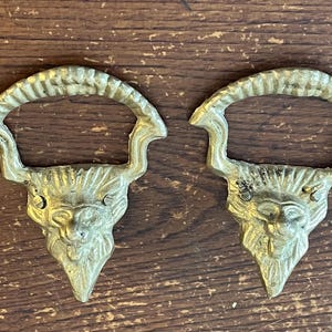 May include: Two gold-toned metal lion head door handles with a ring pull. The handles are detailed with a textured mane and a stylized lion face.