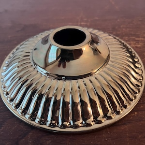 May include: A gold-toned metal lamp finial with a fluted design. The finial has a round top with a hole in the center.
