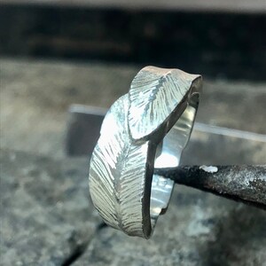 May include: A silver ring with a leaf design. The ring is textured and has a polished finish.
