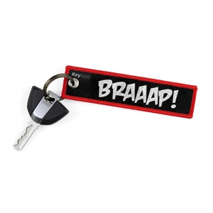 May include: Black and red keychain with the word "BRAAAP!" in white lettering. The keychain is attached to a silver key.