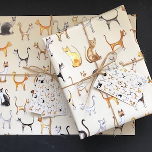 A pack of wrapping paper in our illustrated cats design on a cream background, pack includes 2x sheets and 2x gift tags, picture shows a wrapped present tied with Kraft string with the label and bow on top