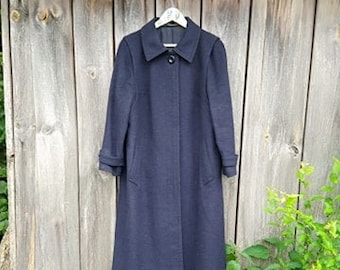 May include: A dark blue wool coat with a classic collar and button closure. The coat has a long, straight silhouette and is hanging on a wooden hanger.