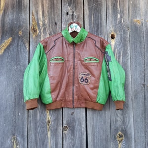 May include: A brown and green leather jacket with a zip fastening. The jacket has a Route 66 patch on the front and the words "Route 66" on the sleeves.