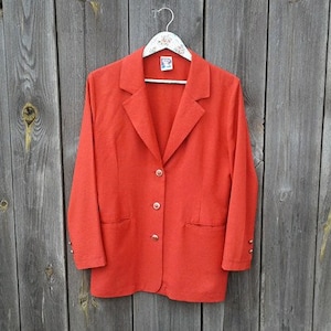 May include: A red blazer with a single-breasted closure and four buttons. The blazer has two pockets on the front and a notched collar.