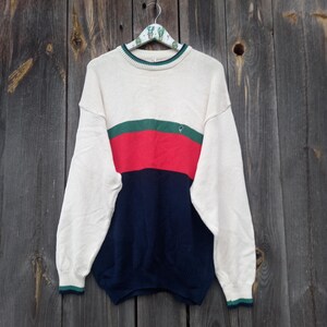 Könnte beinhalten: Ein cremefarbener Pullover mit einem Farbblok-Design in Grün, Rot und Blau. Der Pullover hat einen Rundhalsausschnitt und lange Ärmel.