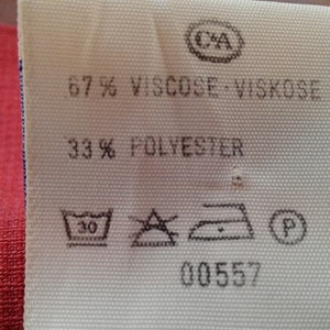 May include: White fabric label with black text and symbols. The label reads "67% Viscose - Viskose 33% Polyester" and includes care instructions. The label also has a number "00557" printed on it.