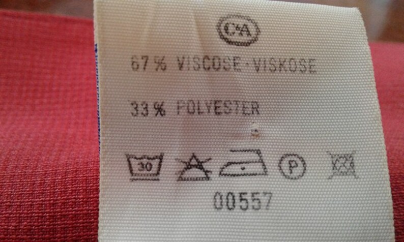 May include: White fabric label with black text and symbols. The label reads "67% Viscose - Viskose 33% Polyester" and includes care instructions. The label also has a number "00557" printed on it.