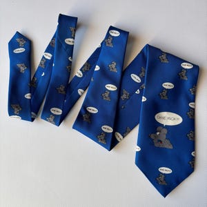 Puede incluir: Una corbata azul con un patrón repetido de un ratón gris en una burbuja de diálogo. La corbata también presenta la frase alemana "OHNE MICH!!!" en una burbuja de diálogo. La corbata es de tela lisa.