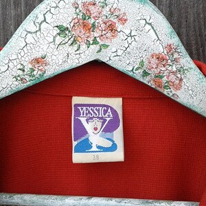 May include: Red blazer with a Yessica brand label. The label features a purple background with a stylized Y and a woman's face. The label also includes the size 38.