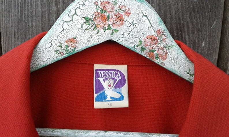 May include: Red blazer with a Yessica brand label. The label features a purple background with a stylized Y and a woman's face. The label also includes the size 38.