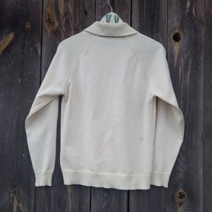 Puede incluir: Un su&eacute;ter blanco de manga larga con cuello. El su&eacute;ter tiene un dobladillo y pu&ntilde;os de canal&eacute;.