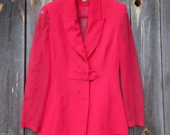 May include: A bright red blazer with a notched lapel and a single-button closure. The blazer features a tailored fit and sheer sleeves, hanging on a wooden hanger against a weathered wood background. A classic piece of outerwear.