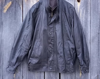 Puede incluir: Una chaqueta de cuero marrón oscuro con cierre de cremallera y botones. La chaqueta tiene un cuello alto y dos bolsillos en la parte delantera.