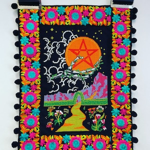 Könnte beinhalten: Ein schwarzer Wandbehang aus Stoff mit einem bunten bestickten Rand. Die Mitte zeigt ein Kreuzstich-Design eines fünfzackigen Sterns in einem Kreis, umgeben von Wolken und einer Landschaft.