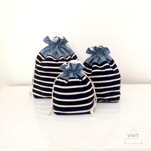 May include: Three drawstring bags in varying sizes. The bags feature a navy blue and white striped pattern on the main body, with a solid light blue gathered top. Each bag has a white drawstring closure.
