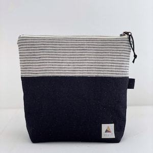 May include: A small, rectangular pouch with a zipper closure. The top half features horizontal gray and white stripes, while the bottom half is solid black. A small tag with the word "VIVIT" is on the lower right corner.