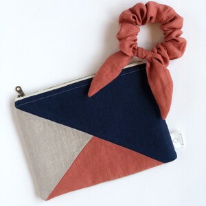 May include: A geometric-patterned pouch with a matching scrunchie. The pouch features a navy blue, tan, and rust-colored design with a zipper closure. The scrunchie is rust-colored and has long, flowing ties.