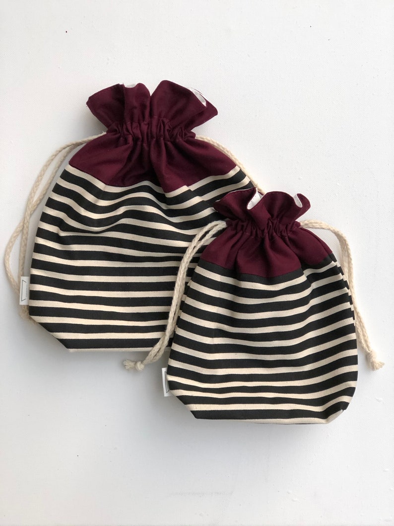 May include: Two drawstring bags with a striped pattern in black and off-white. The top section of each bag is a solid burgundy color. The bags have a natural-colored drawstring closure.