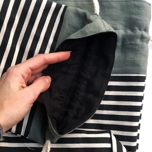 May include: A black and white striped tote bag with a drawstring closure. The bag has a solid gray-green top and a black interior lining. A white rope drawstring is visible.