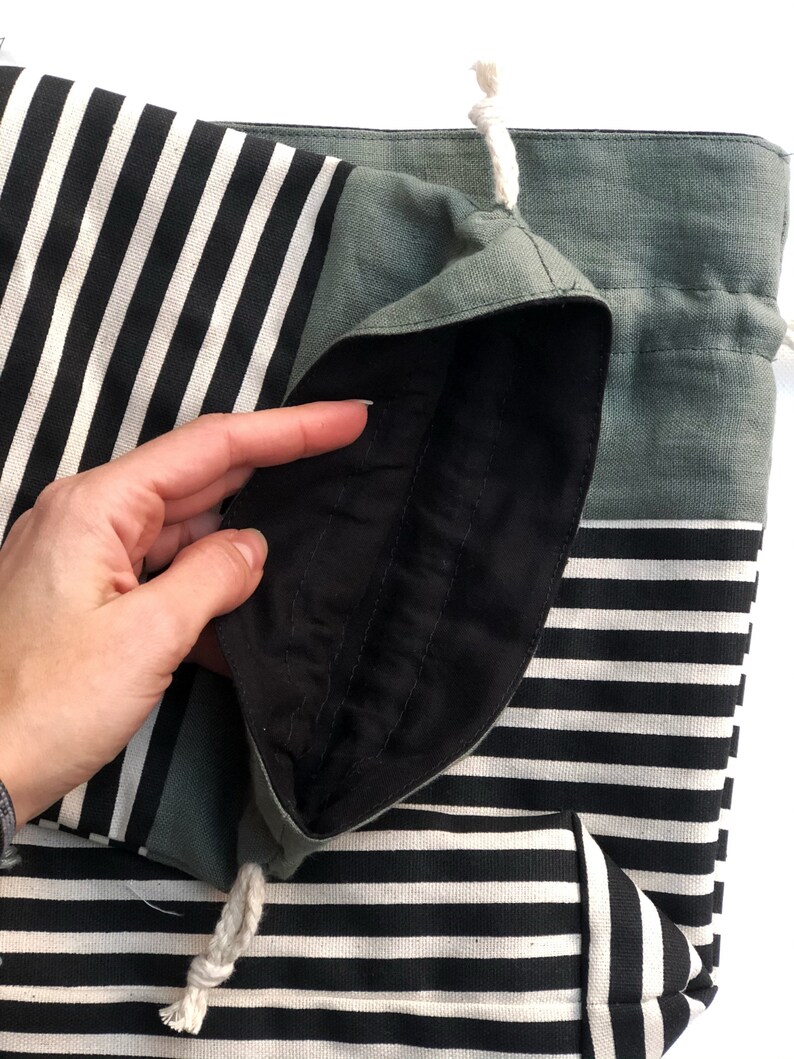 May include: A black and white striped tote bag with a drawstring closure. The bag has a solid gray-green top and a black interior lining. A white rope drawstring is visible.