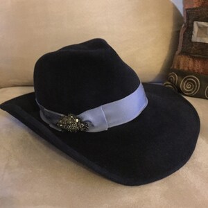 May include: A black felt fedora hat with a wide brim and a light blue ribbon. The hat has a decorative pin with rhinestones.