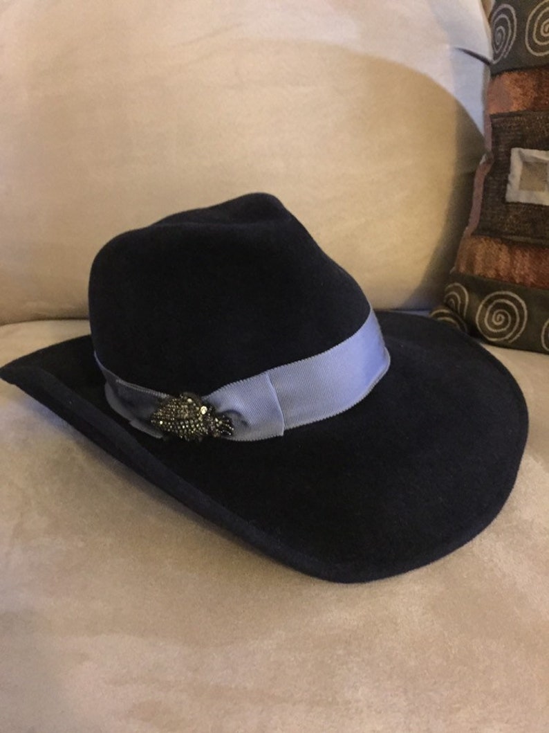 May include: A black felt fedora hat with a wide brim and a light blue ribbon. The hat has a decorative pin with rhinestones.