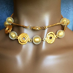 Può includere: Una collana d'oro con perline bianche opache e maglie a spirale dorate. La collana è su un manichino.