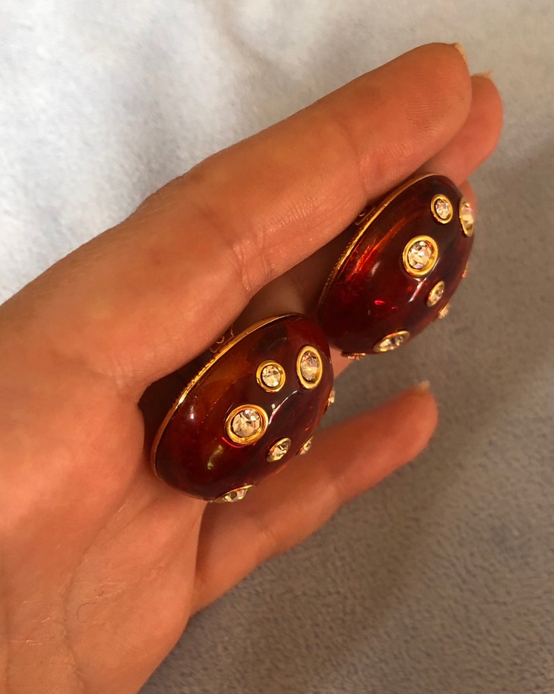 May include: A pair of red and gold tone clip-on earrings with clear rhinestones.