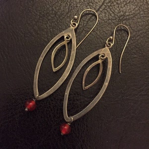 Può includere: Un paio di orecchini pendenti in argento con una perla rossa in fondo a ogni orecchino. Gli orecchini hanno la forma di un ovale con un ovale più piccolo tagliato al centro.