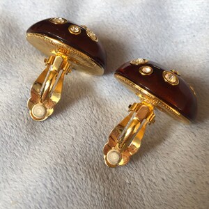 May include: A pair of gold tone mushroom-shaped clip-on earrings with clear rhinestones.