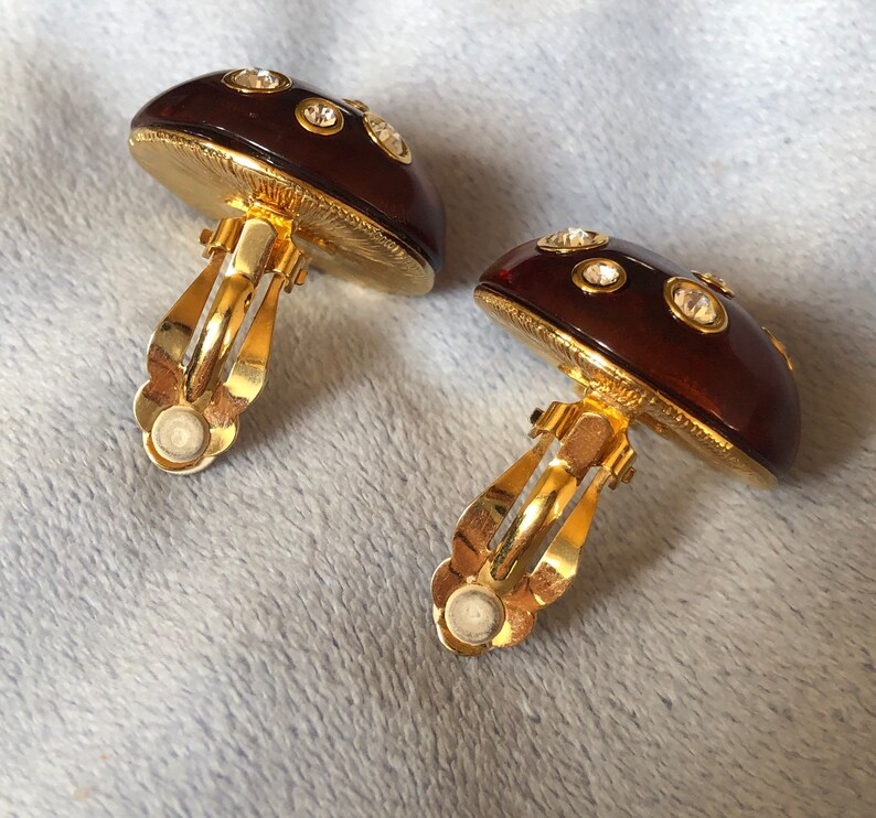 May include: A pair of gold tone mushroom-shaped clip-on earrings with clear rhinestones.